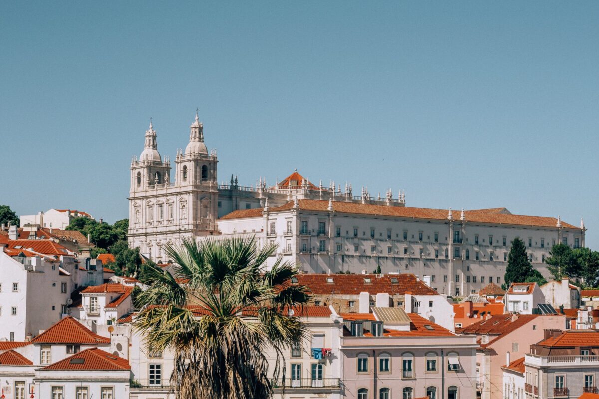 A large white building with red roofs and palm trees - best rental yields in lisbon