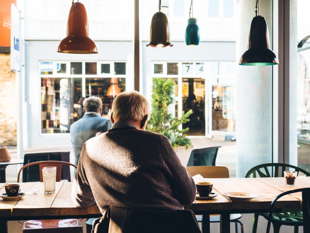 Un homme âgé est assis seul à une table dans un café confortable, en train de lire ou d'écrire  - hote airbnb senior