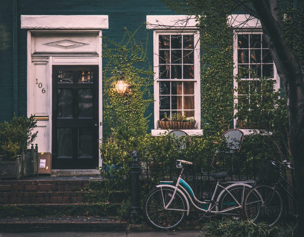 Une maison verte aux murs recouverts de lierre, aux fenêtres bordées de blanc et à la porte d'entrée noire - louer residence principale