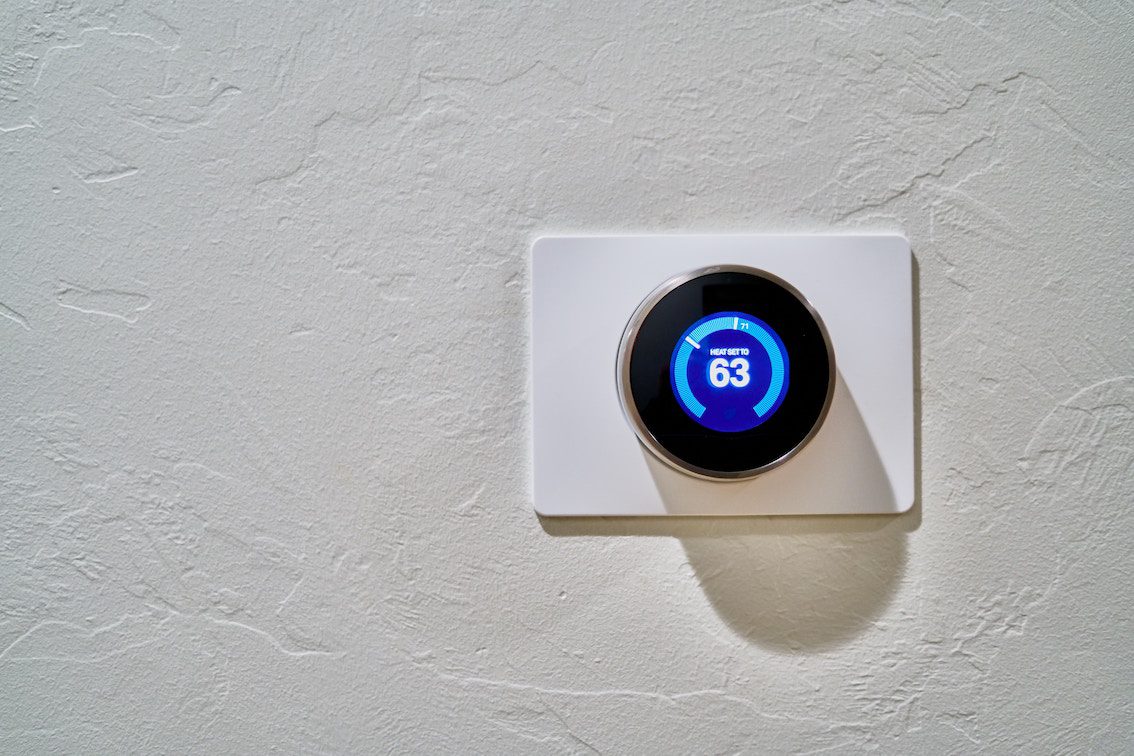A modern digital thermostat is mounted on a textured white wall - airbnb smart homes