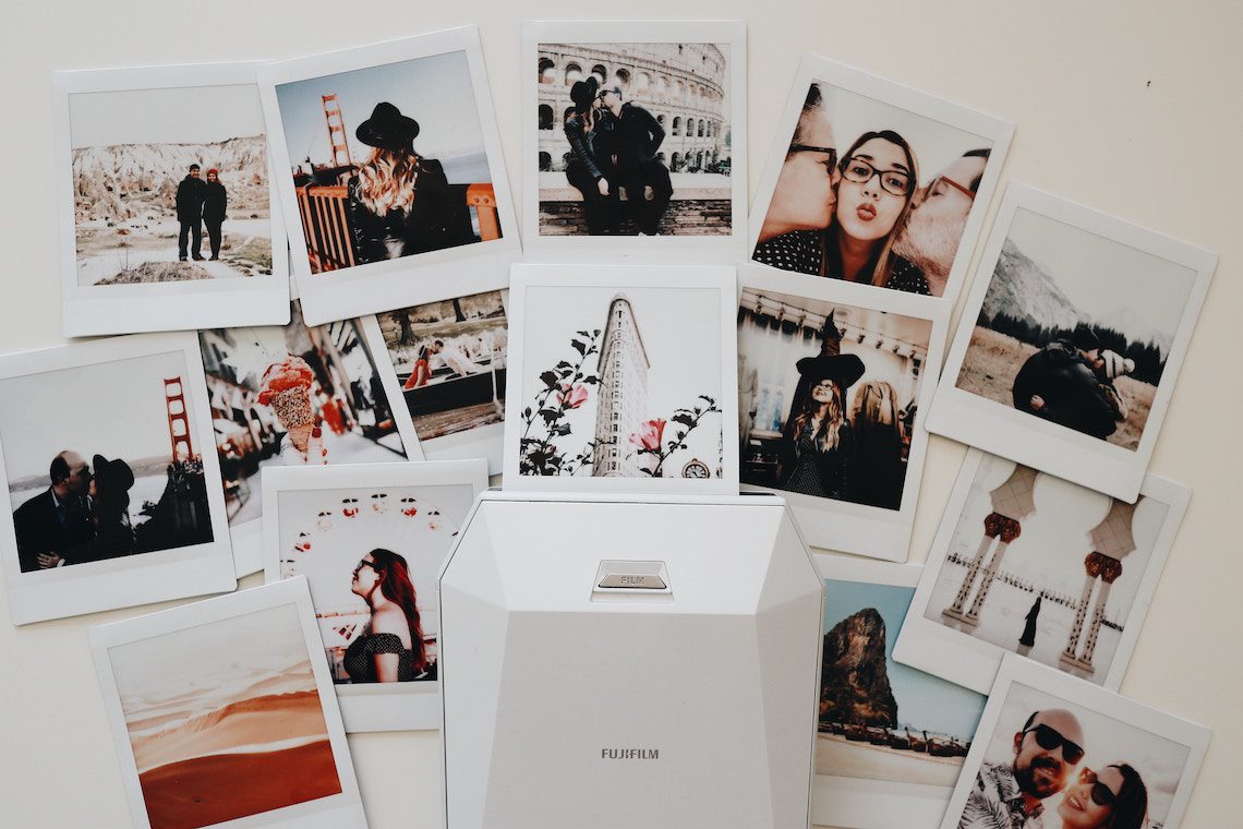 Une imprimante de photos instantanées Fujifilm est posée sur une table, entourée de photos de style polaroïd représentant des couples, des scènes de voyage et des paysages - airbnb résidence principale