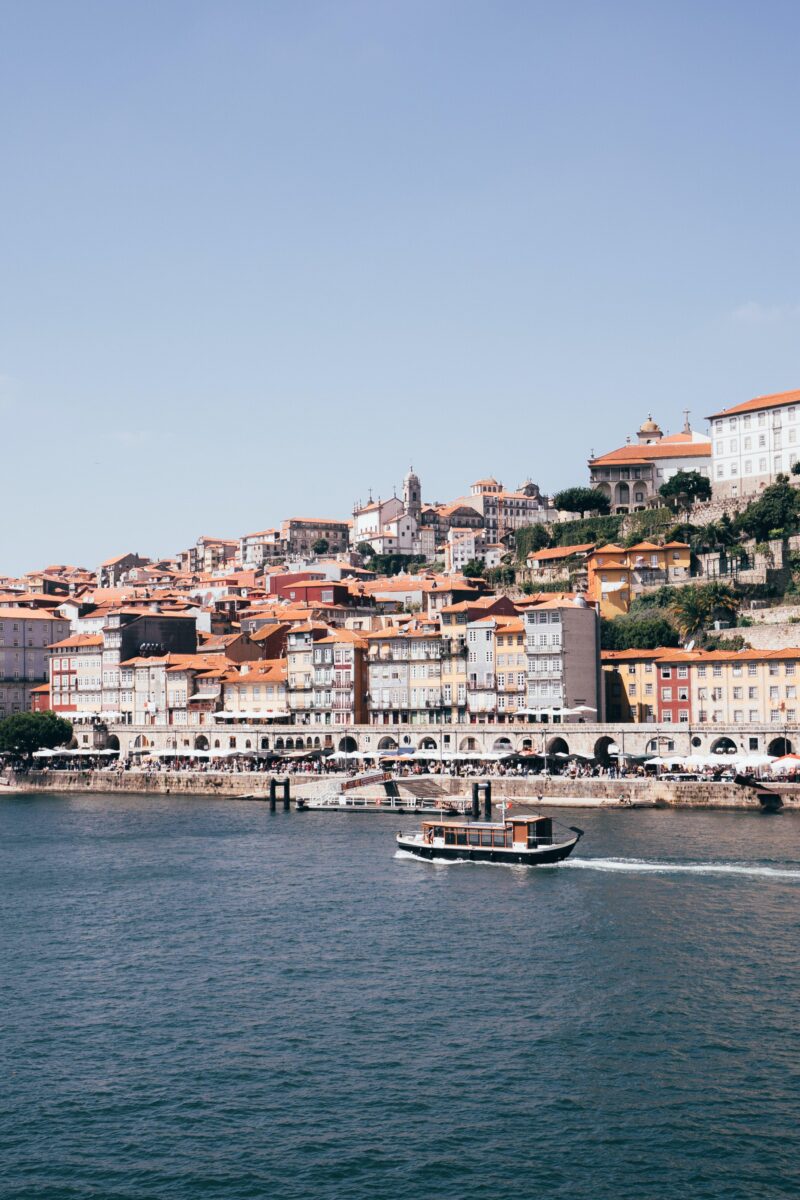 A small boat moves along the Douro River with Porto’s colorful hillside buildings in the background - Porto city break