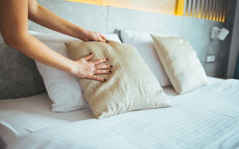 Mains ajustant un coussin sur un lit soigneusement préparé dans une chambre moderne de location avec services.