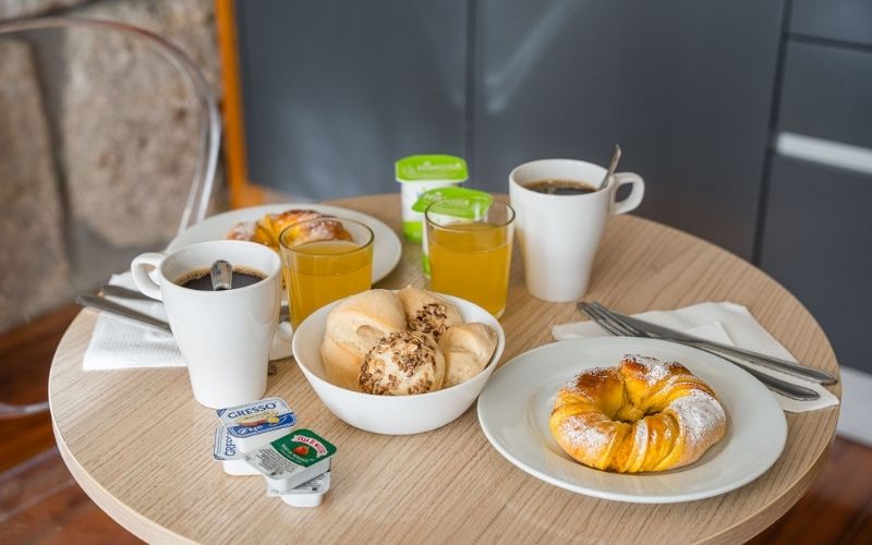 Cómo obtienen los hoteles la mayor cantidad de ingresos - Servicio de habitaciones – Desayuno continental en una habitación de GuestReady con café, jugo de naranja, pasteles, panecillos y yogur sobre una mesa redonda pequeña.