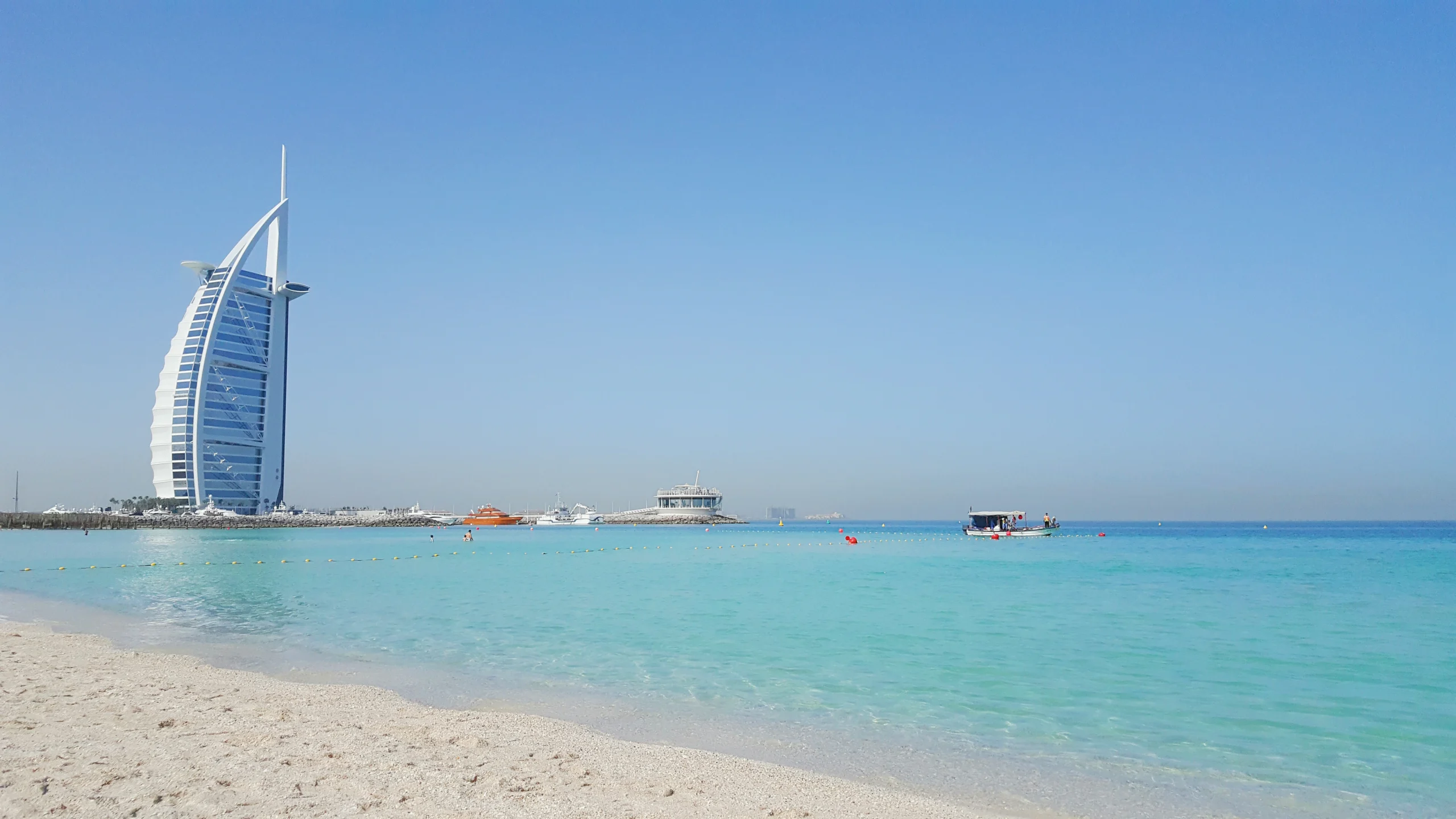 Burj Al Arab rising beside a sandy beach and clear turquoise sea in Dubai.