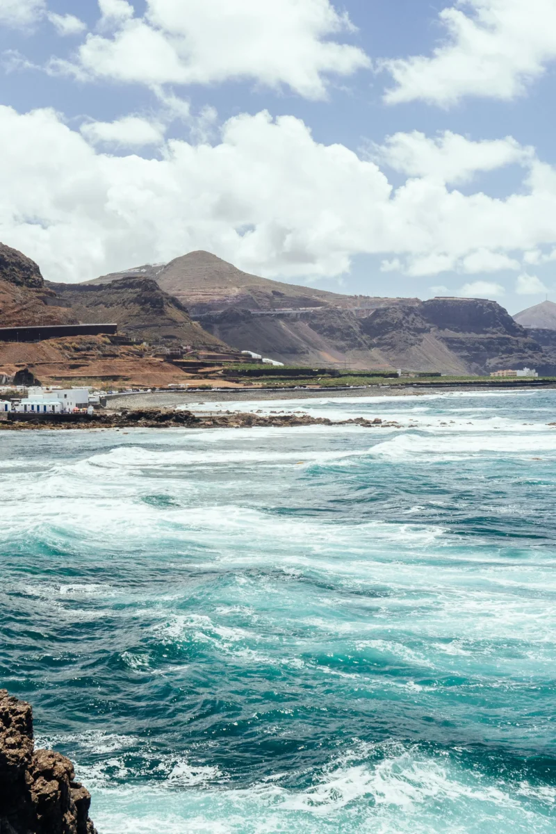 Costa escarpada de La Palma con olas turquesas, rocas y montañas bajo un cielo nublado - Gestión apartamentos turísticos La Palma, GuestReady