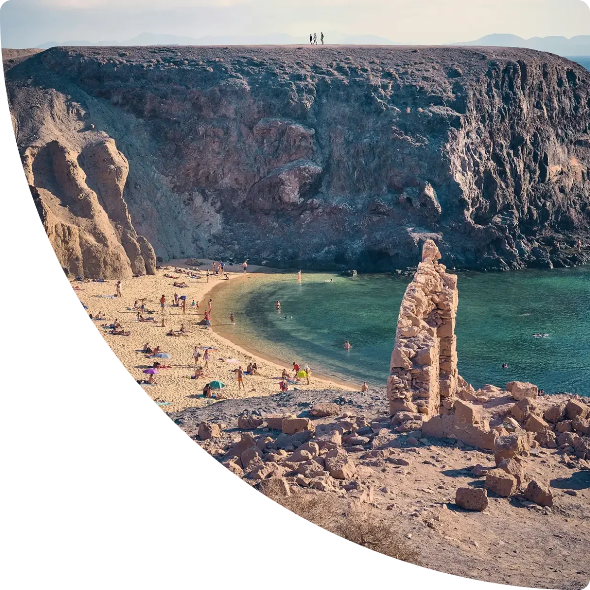Turquoise-water cove surrounded by cliffs, with people on the beach - Airbnb management in Lanzarote, GuestReady