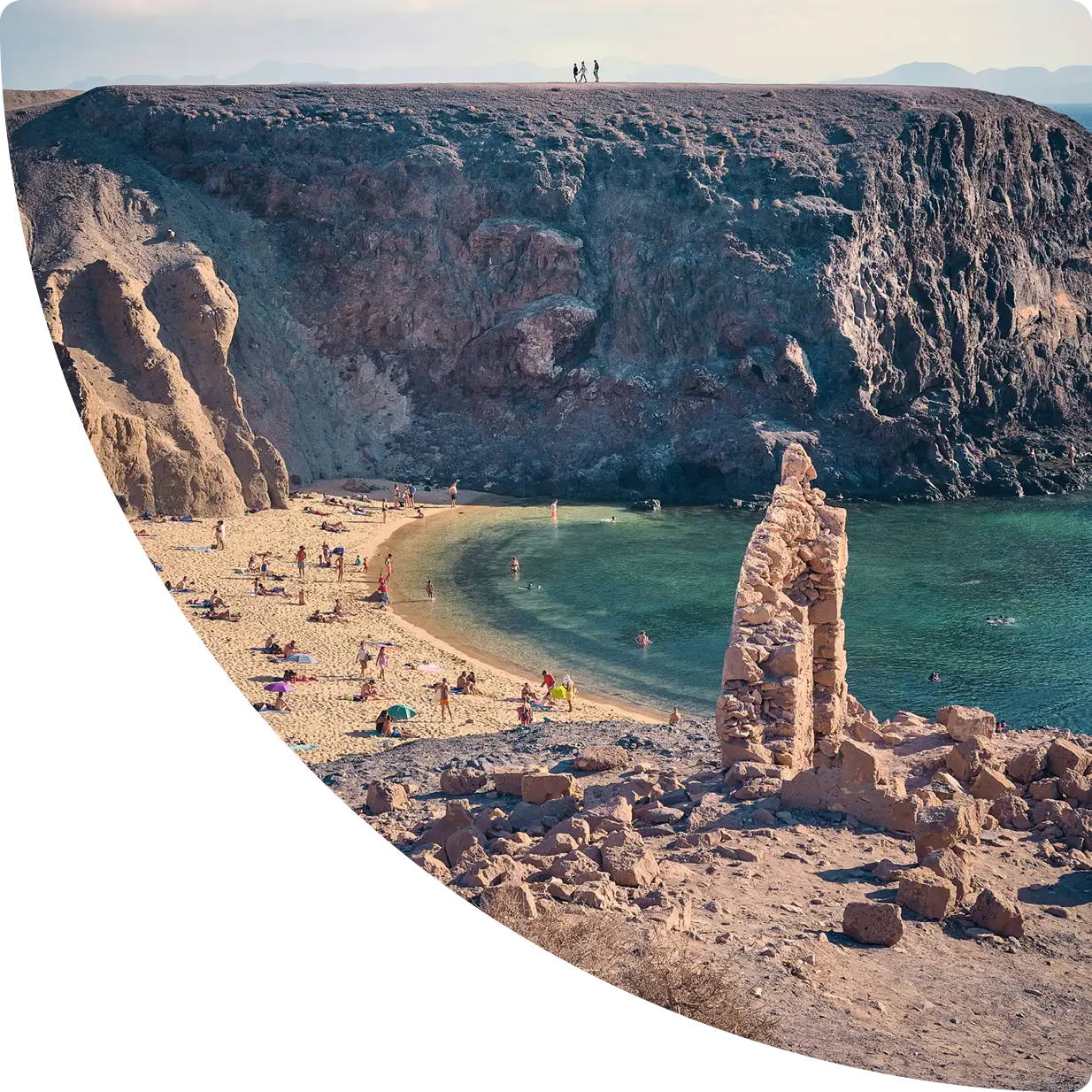 Cala de aguas turquesas rodeada de acantilados, con gente en la playa - gestión apartamentos turísticos Lanzarote, GuestReady.