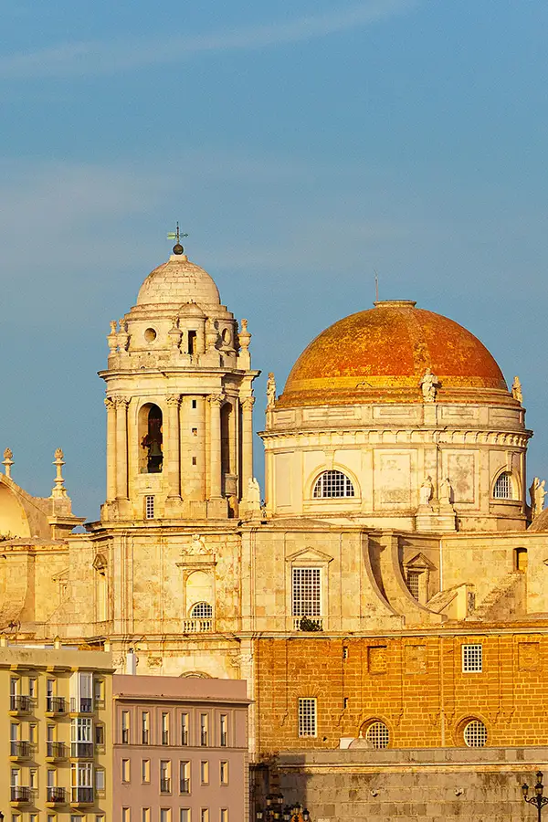 Sunlit cathedral with a golden dome and bell tower against a clear blue sky - Airbnb management in Cádiz, GuestReady