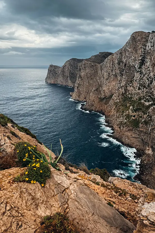 Dramatic sea cliffs above dark blue water under a cloudy sky, viewed from a rocky lookout - Huelva