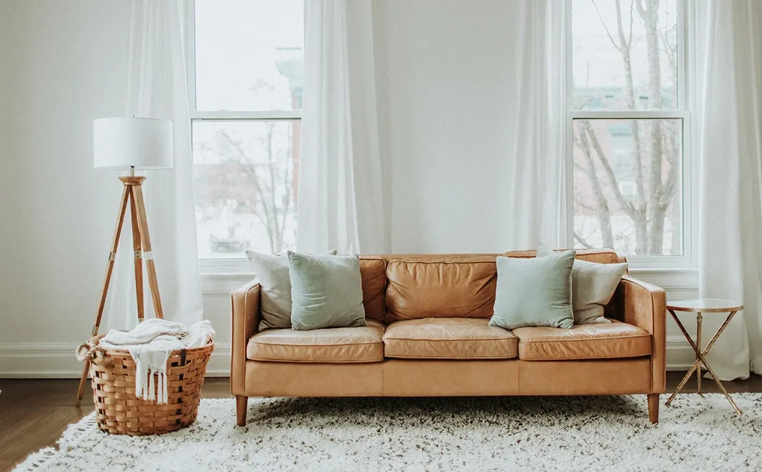 Salón acogedor con sofá color camel, cojines suaves y grandes ventanales con cortinas ligeras