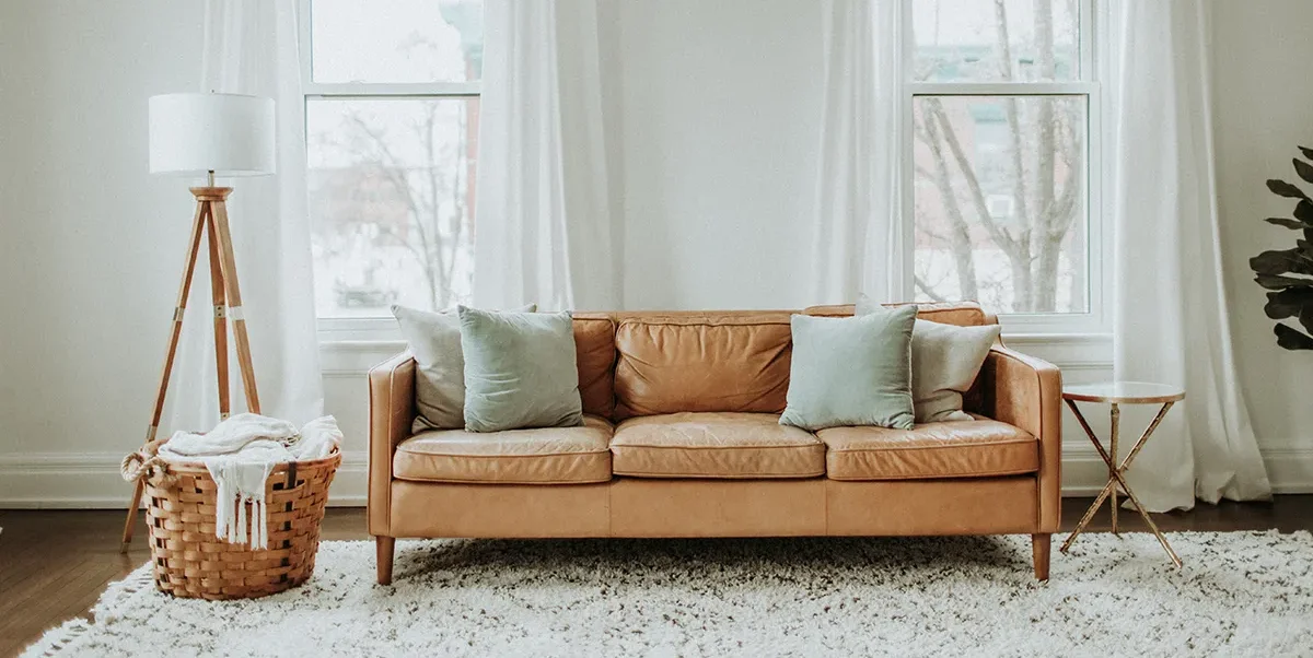 Cozy living room with a tan sofa, soft cushions, and large windows with sheer curtains