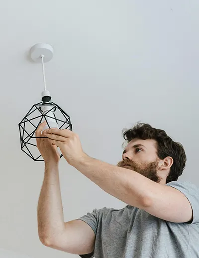 Hombre instalando una lámpara de techo con estructura metálica en una habitación luminosa - Daños para anfitriones Airbnb