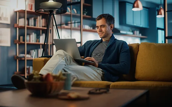 Hombre en el sofá usando un portátil para encontrar una plataforma digital para las reparaciones y el mantenimiento de su propiedad.