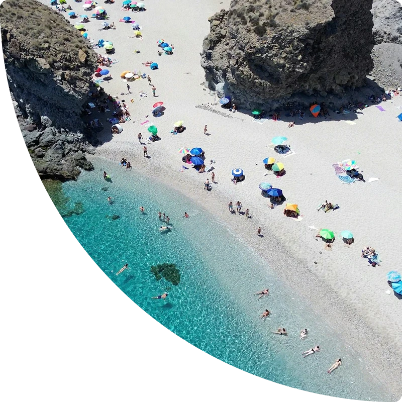 Coastal cove with clear water and sunbathers on a sandy beach, airbnb management andalusia